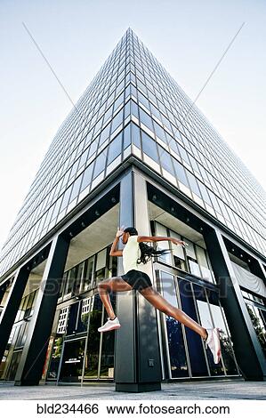 Stock Photograph - Black woman running and jumping on city sidewalk. Fotosearch