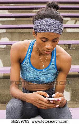 Black woman sitting on bleachers texting on cell phone View Large Photo Image Stock Image - Black woman sitting on bleachers texting on cell phone. Fotosearch