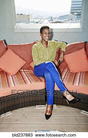Stock Image - Black woman sitting on rooftop sofa. Fotosearch