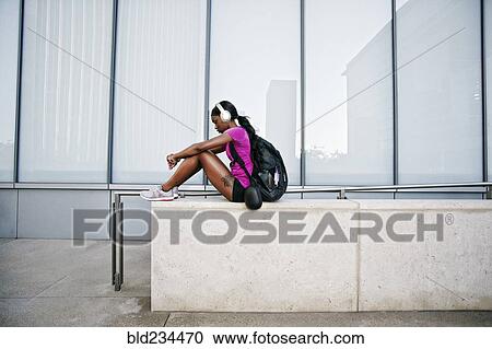Black woman sitting on urban wall listening to headphones View Large Photo Image Stock Image - Black woman sitting on urban wall listening to headphones. Fotosearch