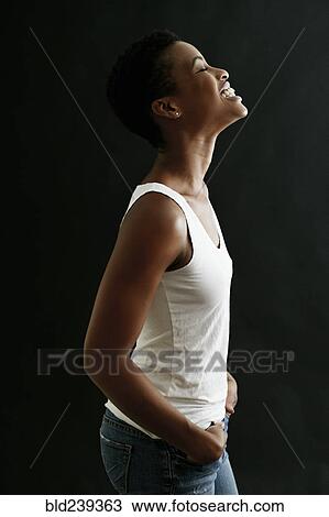 Stock Image - Black woman standing and laughing with hands in pockets. Fotosearch