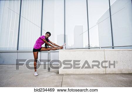 Stock Photo - Black woman stretching leg on urban wall. Fotosearch
