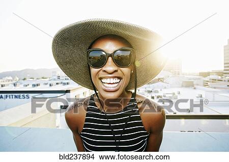 Picture - Black woman wearing sun hat and sunglasses on rooftop. Fotosearch