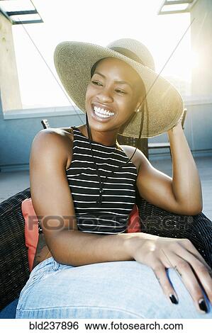 Stock Photograph - Black woman wearing sun hat on rooftop. Fotosearch
