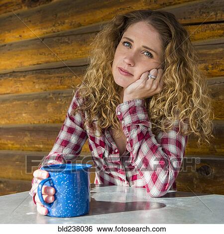 Stock Photograph - Bored Caucasian woman leaning table holding coffee cup. Fotosearch