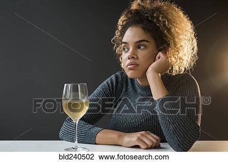 Stock Image - Bored Mixed Race woman wearing sweater drinking wine. Fotosearch