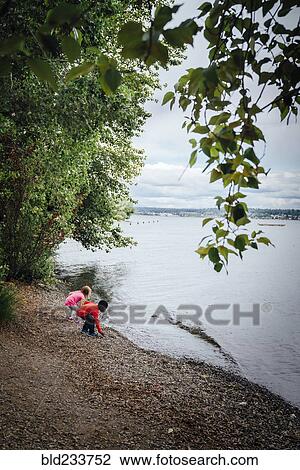 Stock Image - Boy and girl crouching at river. Fotosearch
