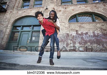 Stock Photograph - Boyfriend giving girlfriend piggyback ride in urban area. Fotosearch