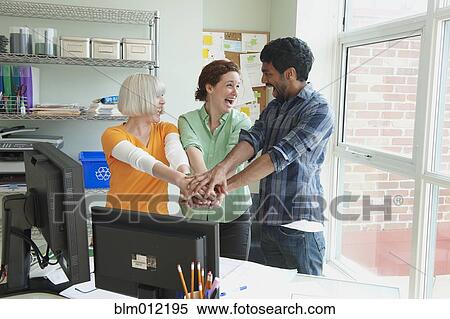 Stock Photography - Business people holding hands together in office. Fotosearch