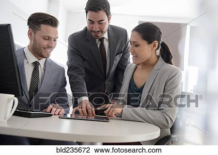 Stock Image - Business people talking in office using digital tablet and computer. Fotosearch