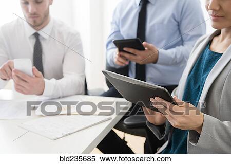 Stock Photography - Business people using digital tablets and cell phone in office. Fotosearch