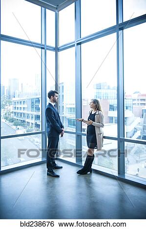 Businessman and businesswoman talking near window View Large Photo Image Stock Photograph - Businessman and businesswoman talking near window. Fotosearch