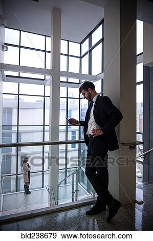 Stock Photo - Businessman texting on cell phone near staircase. Fotosearch
