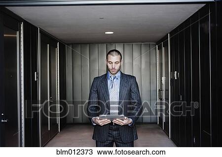 Stock Image - Businessman using digital tablet in corridor. Fotosearch