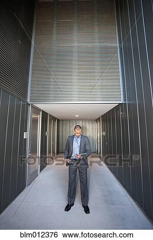Stock Photograph - Businessman using digital tablet in corridor. Fotosearch