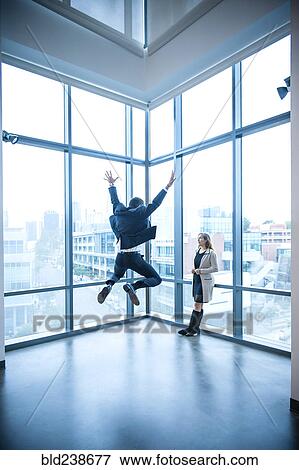 Businesswoman watching businessman celebrating near window View Large Photo Image Stock Photo - Businesswoman watching businessman celebrating near window. Fotosearch