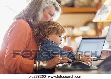 Stock Image - Caucasian baby boy in lap of grandmother using computer. Fotosearch