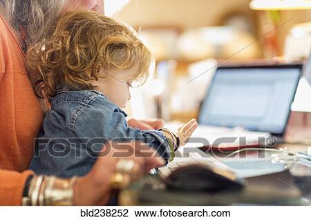 Stock Image - Caucasian baby boy in lap of grandmother using computer keyboard. Fotosearch