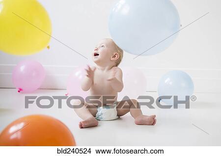 Picture - Caucasian baby boy sitting on floor watching balloons. Fotosearch