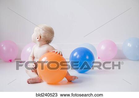 Stock Image - Caucasian baby boy sitting on floor with balloons. Fotosearch