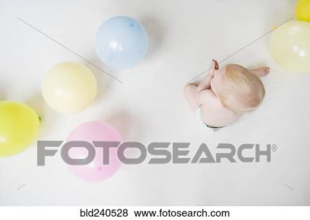 Stock Photo - Caucasian baby boy sitting on floor with balloons. Fotosearch