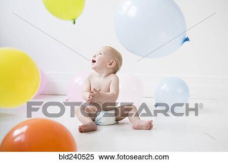 Stock Photography - Caucasian baby boy sitting on floor watching balloons. Fotosearch