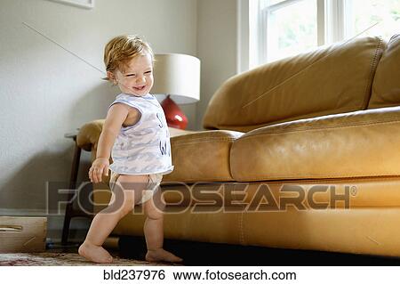 Stock Photograph - Caucasian baby boy walking near sofa. Fotosearch