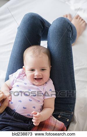 Stock Image - Caucasian baby girl laying on legs of mother. Fotosearch
