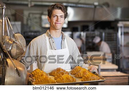 Stock Photograph - Caucasian baker carrying tray of croissants in bakery. Fotosearch