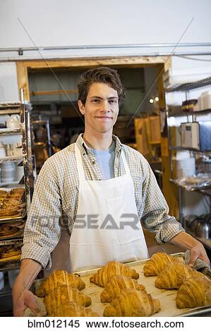 Stock Photography - Caucasian baker carrying tray of croissants in bakery. Fotosearch