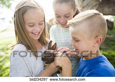 Stock Photo - Caucasian boy and girls petting rabbit. Fotosearch