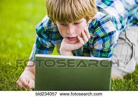Stock Photo - Caucasian boy kneeling in grass using laptop. Fotosearch