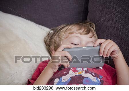 Stock Photograph - Caucasian boy laying on sofa watching cell phone. Fotosearch