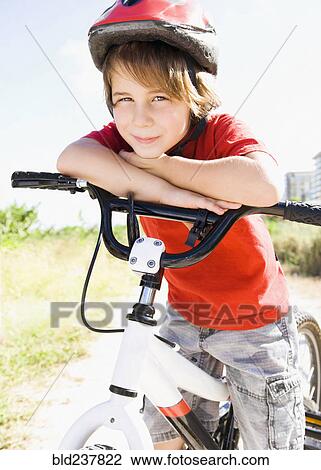 Stock Image - Caucasian boy leaning on bicycle handlebar. Fotosearch