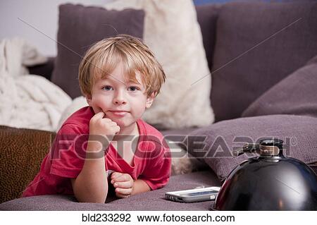 Stock Image - Caucasian boy leaning on sofa near cell phone. Fotosearch