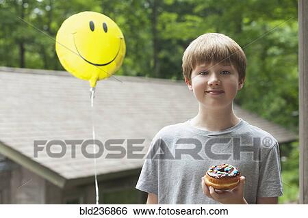 Stock Photograph - Caucasian boy posing with smiley face balloon and donut. Fotosearch