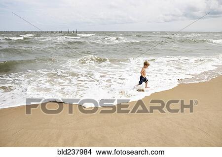 Picture - Caucasian boy running in waves at beach. Fotosearch