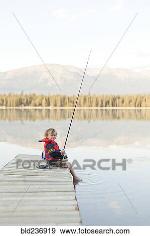 Stock Photo - Caucasian boy sitting on dock at lake holding fishing rod. Fotosearch