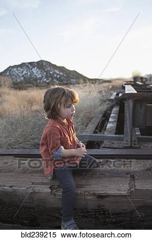 Stock Photography - Caucasian boy sitting on wood outdoors. Fotosearch