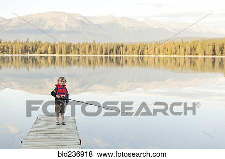 Stock Photo - Caucasian boy standing on dock at lake holding fishing rod. Fotosearch