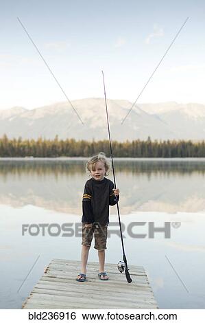 Stock Photograph - Caucasian boy standing on dock at lake holding fishing rod. Fotosearch