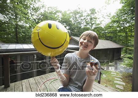 Caucasian boy with messy face holding smiley face balloon and eating donut View Large Photo Image Stock Photo - Caucasian boy with messy face holding smiley face balloon and eating donut. Fotosearch