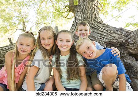Stock Photography - Caucasian boys and girls posing near tree. Fotosearch
