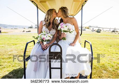 Stock Image - Caucasian brides kissing in golf cart. Fotosearch