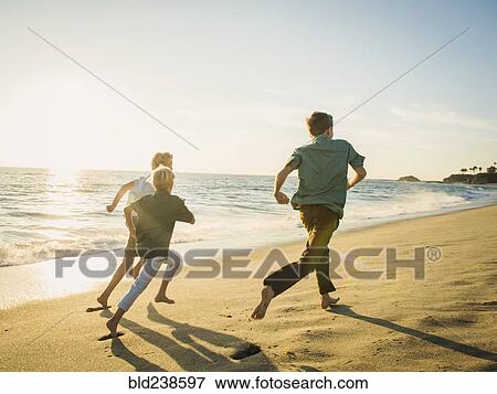Stock Photo - Caucasian brothers running on beach. Fotosearch
