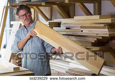 Stock Photo - Caucasian carpenter eyeballing wooden plank in workshop. Fotosearch