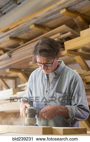 Stock Image - Caucasian carpenter sanding wood in workshop. Fotosearch