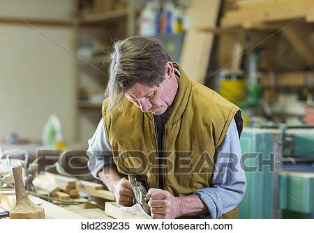 Stock Photography - Caucasian carpenter sanding wood in workshop. Fotosearch