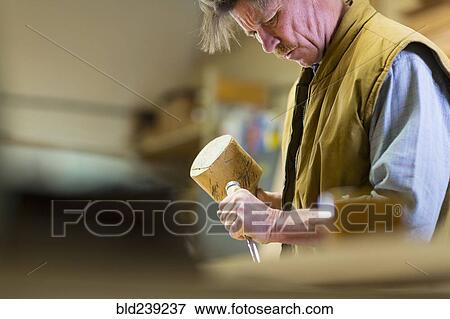 Stock Photo - Caucasian carpenter using mallet and chisel in workshop. Fotosearch