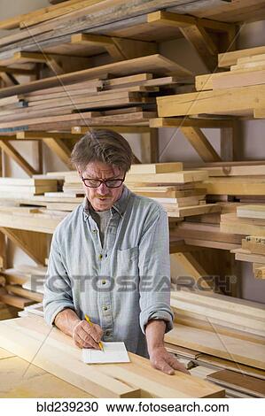 Stock Image - Caucasian carpenter writing on notepad in workshop. Fotosearch